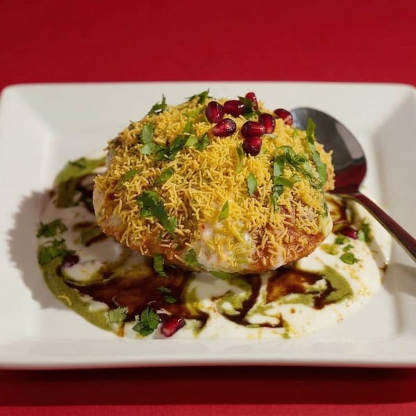 Indian chaat with sev, pomegranate seeds, and cilantro on a white plate with sauces.
